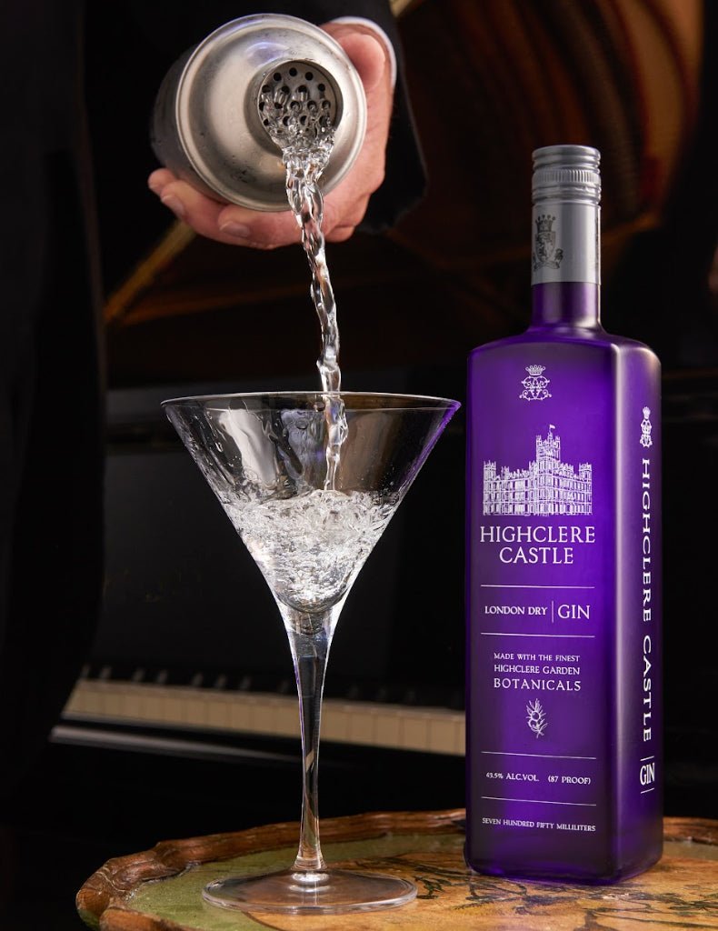 Highclere Castle Gin bottle beside a martini glass being filled with gin from a cocktail shaker. The gin, produced at Highclere Castle, the real Downton Abbey, is highlighted in an elegant setting.
